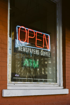 A shop shows an open sign with coffee and newspapers displayed in the window while the ATM is lit...