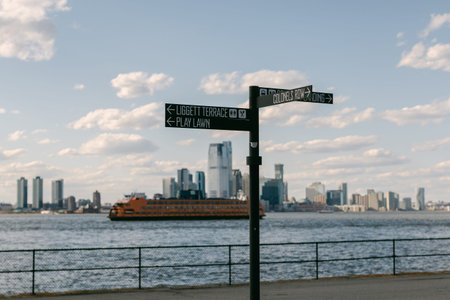 A sign with directions stands by the waterfront. In the background, tall buildings rise against a...