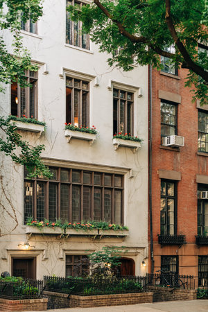 A tall building stands on the street with several windows. Flowers decorate the window sills. A...