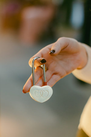A person is holding a heart-shaped lock with two interlocking rings. The sun is shining, and people are visible in the background. This moment is light and casual.の写真素材