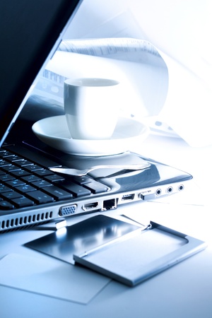 Businessman table with documents, papers, contracts, black lap-top and a cup of coffee  On the foreground a business card holder and visit cards lie on the tableの写真素材