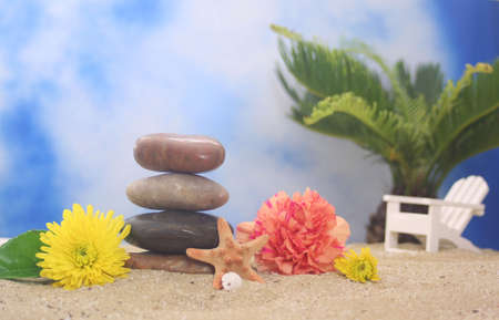 Balanced Stones and Flowers with Sea Shells on Beach With Chair and Palm Tree in Backgroundの写真素材
