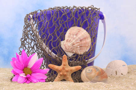 Sand Pail With Net and Sea Shells on Sand With Blue and White Backgroundの写真素材
