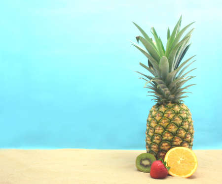 Pineapple With Kiwi and Orange on Sand With Blue Backgroundの写真素材
