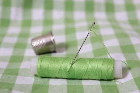 Spool of Light Green Thread, Thimble and Needle on Green Checkered Fabricの写真素材
