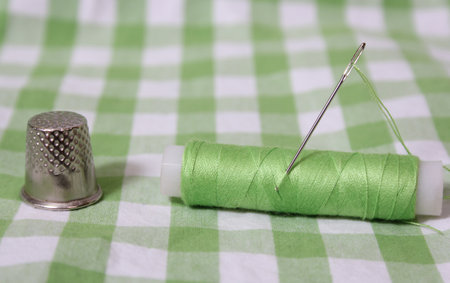 Spool of Light Green Thread, Thimble and Needle on Green Checkered Fabricの写真素材