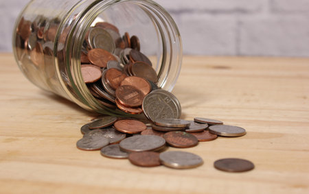 Glass Jar of American Coins on Wooden Table With Brick Wall Background