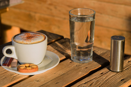 Cappuccino coffee in a white cup. with cinnamone and biscuits.in a glass of water.Coffee flavored drink, cappuccino is made of Italian espresso. It is very fragrant and delicious drink.の写真素材
