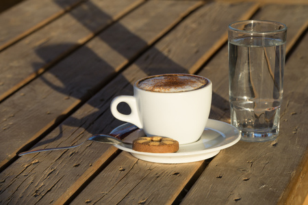 Cappuccino coffee in a white cup. with cinnamone and biscuits.in a glass of water.Coffee flavored drink, cappuccino is made of Italian espresso. It is very fragrant and delicious drink.の写真素材