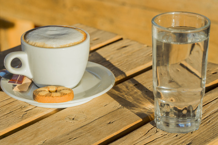 Cappuccino coffee in a white cup. with cinnamone and biscuits.in a glass of water.Coffee flavored drink, cappuccino is made of Italian espresso. It is very fragrant and delicious drink.の写真素材