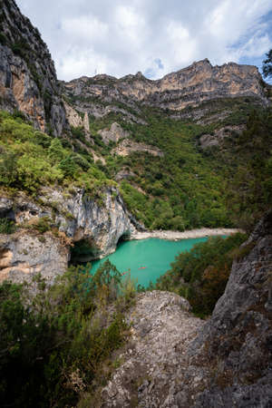 Deep turquoise river at the bottom of a vertical canyon with people kayaking.の写真素材