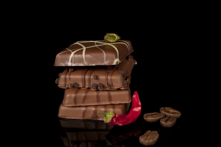 luxurious chocolate with chili pepper and coffee beans on black background