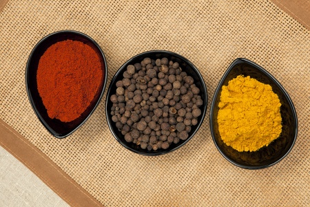 Three black bowls with different spices on brown natural background. Pepper corns, paprika and curry.の写真素材