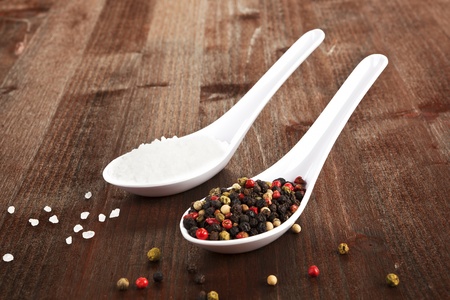 Sal crystals and colorful pepper corns on white spoons on dark wooden background.の写真素材
