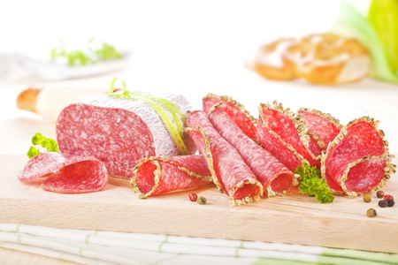 Luxurious salami slices arranged on wooden board with fresh herbs and pepper corns. Culinary eating.の写真素材