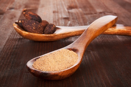 Grated nutmeg in wooden spoon and whole nutmegs on wooden spoon in background on dark wooden background. Culinary aromatic spice.の写真素材