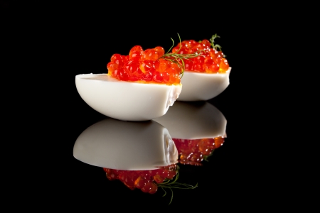 Red caviar in egg decorated with fresh dill isolated on black background with reflection. Luxury food. の写真素材