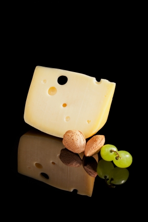 Big emmental piece with almond and grapes isolated on black background with reflection. Culinary cheese.の写真素材