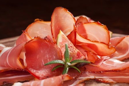 Prosciutto slices arranged on wooden cutting board with fresh herb rosemary and fig  Traditional italian meat background の写真素材