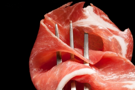 Detail of parma ham on antique fork isolated on black background  Culinary meat concept  Prosciutto の写真素材