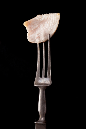 Delicious juicy chicken piece on old fork isolated on black background  Culinary meat eating concept の写真素材