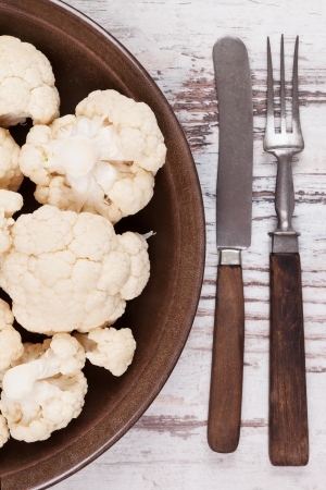 Fresh raw cauliflower on dark brown plate with wooden cutlery on white wooden textured background, top view  Fresh raw vegan and vegetarian eating concept  の写真素材