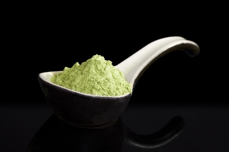 Green wheatgrass powder on ceramic spoon isolated on black background. Alternative medicine concept. Dietary supplementの写真素材