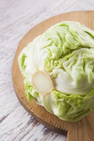 Raw cabbage on wooden cutting board on white wooden background. Healthy summer raw food vegetable eating, country style.の写真素材