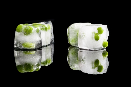 Fresh raw ripe peas frozen in ice cubes isolated on black background. Refreshing fresh summer spring vegetable concept.の写真素材