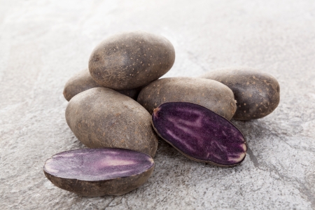 Raw purple culinary potatoes isolated on natural stone background. Healthy vegetable eating.の写真素材