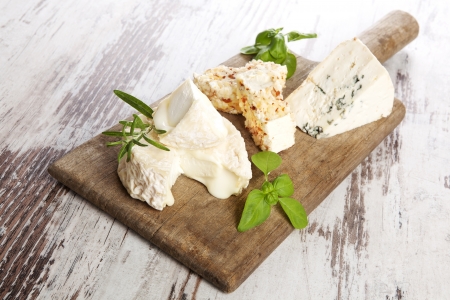 Delicious rustic style cheese still life. Various cheese sorts with fresh herbs on old wooden cutting board on white wooden background. Culinary cheese eating.の写真素材