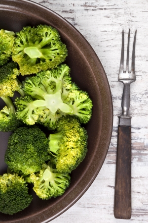 Delicious broccoli on brown plate with fork on white wooden background, top view. Healthy vegetable eating. の写真素材