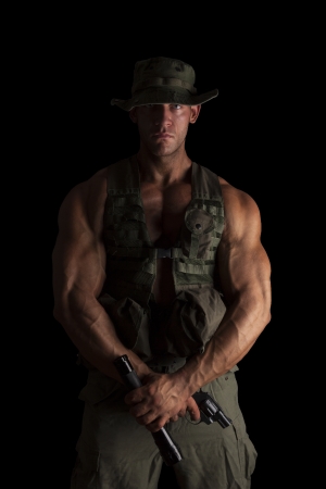 Serious young muscular soldier with gun and flashlight in green uniform standing proud isolated on black background. Army, security and protection.の写真素材