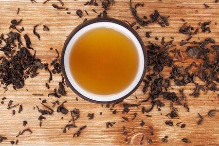 Mug of hot delicious green tea surrounded with dried leaves on wooden background