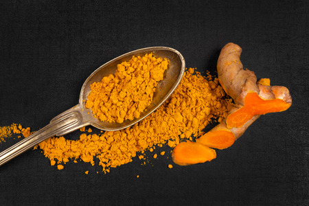 Fresh curcuma root and ground cucrumin powder on black backgroun, top view. Culinary international...