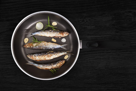 Delicious fresh anchovy fish with fresh rosemary herbs on pan on black wooden background. Culinary healthy seafood cooking.の写真素材
