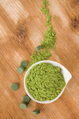Detox. Chlorella pills and wheat grass powder in bowl on brown wooden background. Natural alternative medicine, weight loss and detox.の写真素材