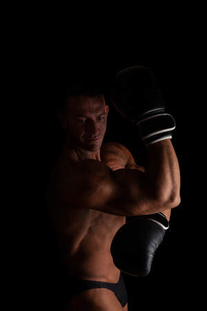 Fighter. Young sexy muscular shirtless man with boxing gloves looking into camera isolated on black background. Sport and fitness.の写真素材