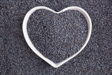 Poppy seed background. Poppy seeds in heart shaped bowl, top view. Healthy eating.の写真素材