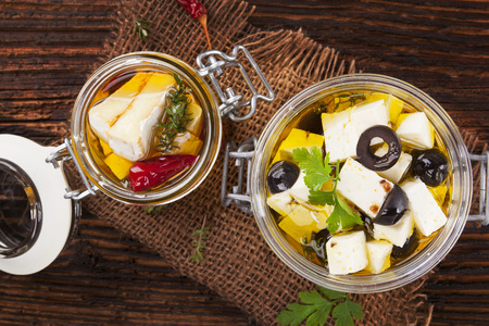 Marinated camembert and greek feat cheese in oil in glass jar on wooden table. Traditional culinary cheese eating.の写真素材