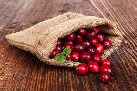 Ripe delicious cranberries in burlap bag on rustic wooden table. Healthy fruit eating.の写真素材