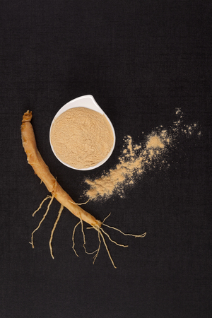 Ginseng root with ginseng powder in bowl on dark background, top view. Traditional eastern natural remedy.の写真素材