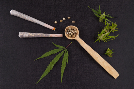Marijuana seeds in wooden spoon with joints, buds and leaves from above. Alternative medicine.の写真素材
