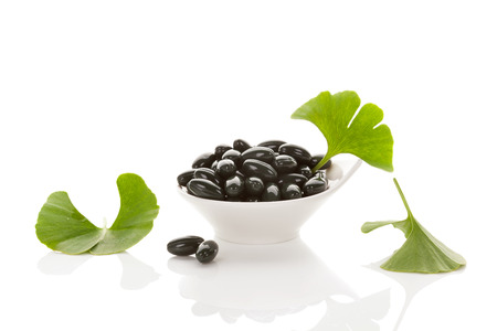 Ginkgo leaves with gel capsules isolated on white background with reflection. Alternative medicine, nutritional supplement, natural remedy. の写真素材