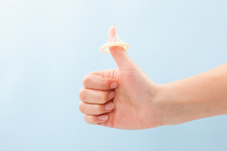 Condom on thumb up gesture. Female hand with thums up and condom on thumb. Safe sex concept. の写真素材