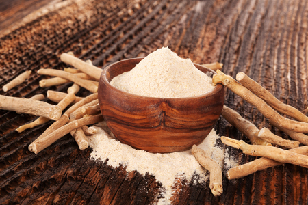 Heap of Ashwagandha powder in wooden bowl  with roots. Superfood remedy.の写真素材