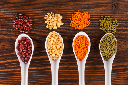 Various fresh legumes in spoons on wooden table, top view. Vegetarian and vegan healthy eating.の写真素材