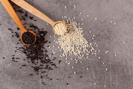 White and black sesame seeds on wooden spoon on grey background.の写真素材