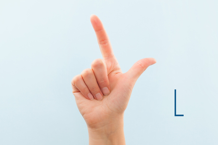 American sign language. Female hand showing letter L isolated on blue background. の写真素材