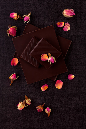 Luxury dark chocolate bar with dried rose on black background. Delicious sweets.の写真素材